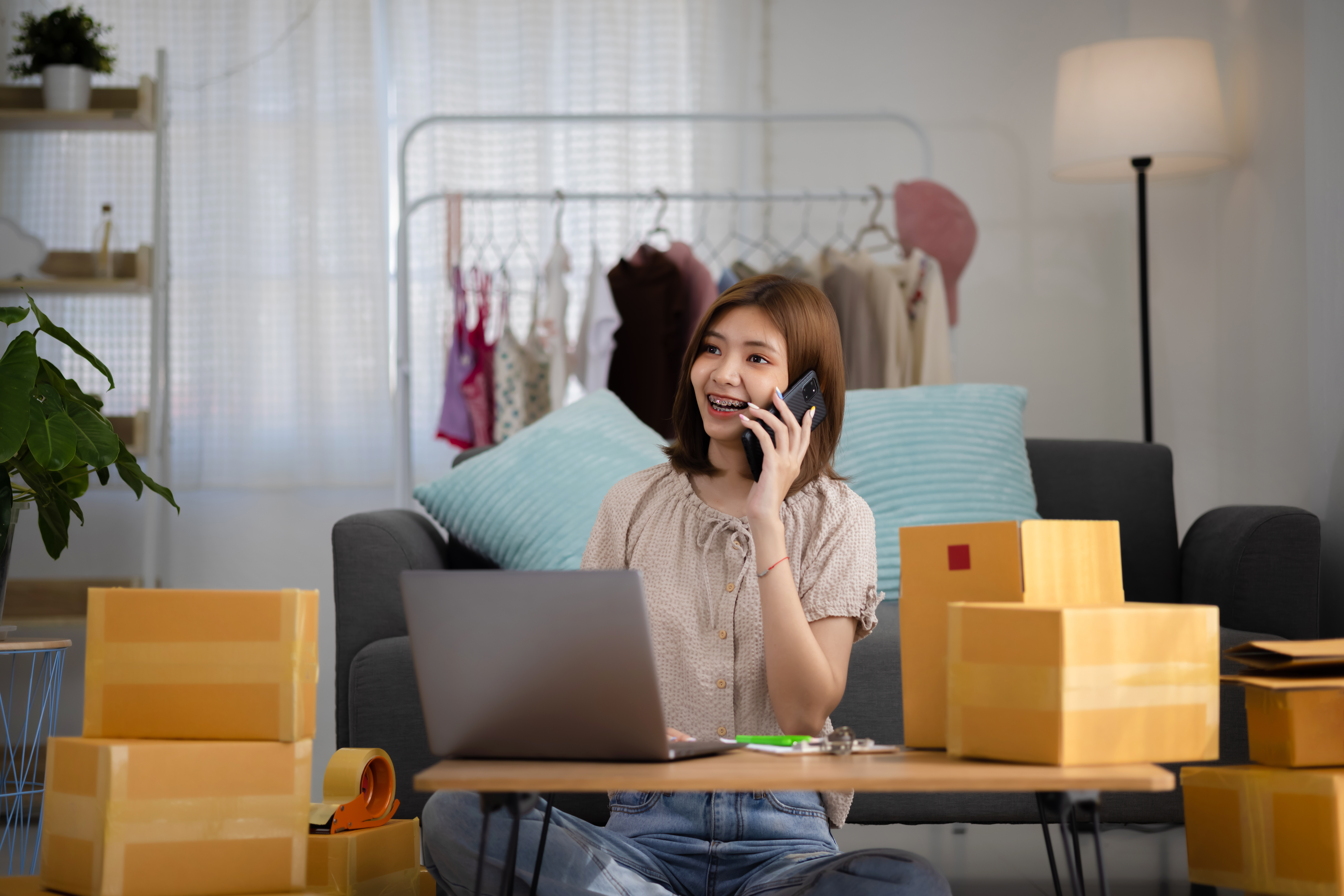 https://img.moneyduck.com/article_attachment/1667969159-smiling-happy-young-asian-woman-entrepreneur-receiving-phone-call-new-sales-order-among-boxes-product-with-laptop-computer.jpg