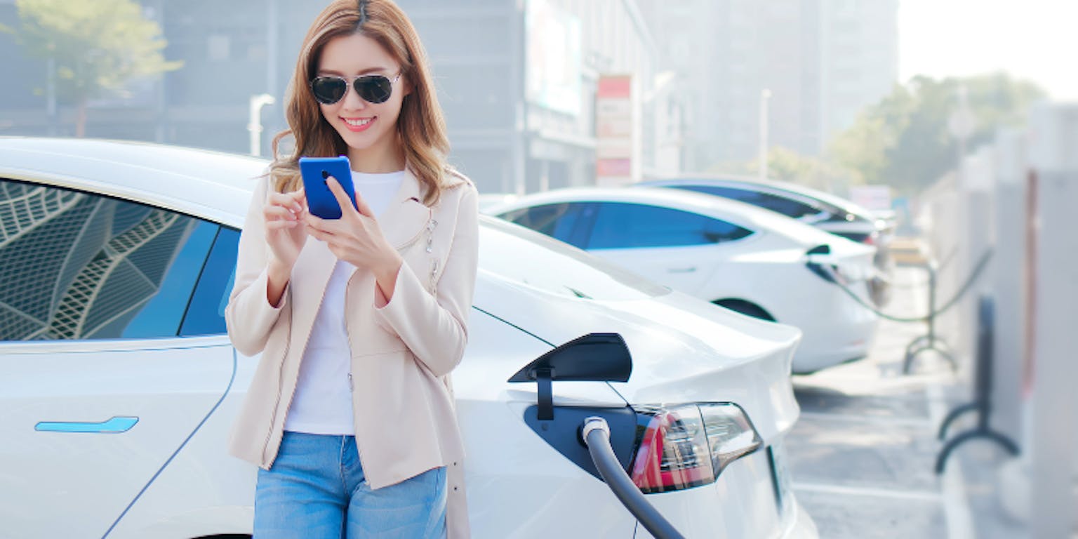 Seorang wanita memegang ponsel di depan mobilnya
